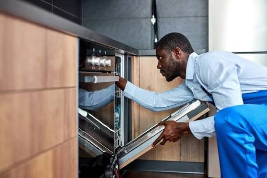 Technician checking the controls of a built-in oven with its door open