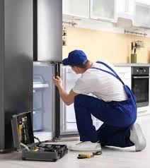 Technician kneeling beside an open refrigerator to inspect its interior